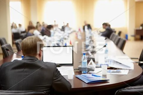 Rear view of speaker at the table with laptop in front presenting his report to Stock Photos