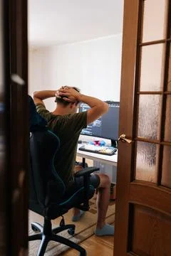 Rear view of stressed programmer sitting in gaming chair in home office, holding 库存照片