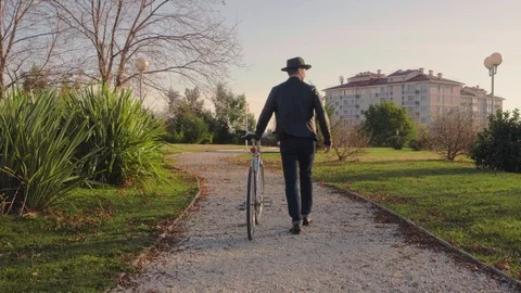 Rear view, stylish man in a hat walking in the Park with a Bicycle. A man with a Video stock 121808043