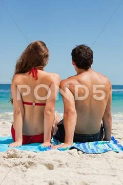 Rear view of a tanned couple sitting on a blue beach towel Stock Photos