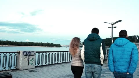 Rear view of three people walking along promenade at sunset. Evening walk 動画素材 132591518