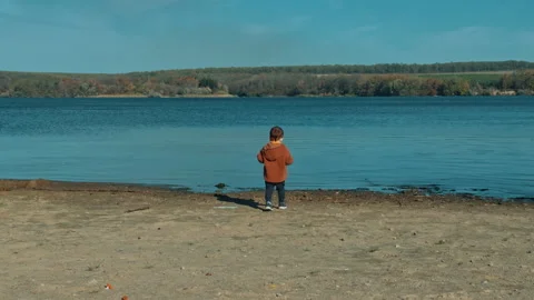 Rear view of a toddler in brown jacket walking to the river.  Stock Footage 254632153