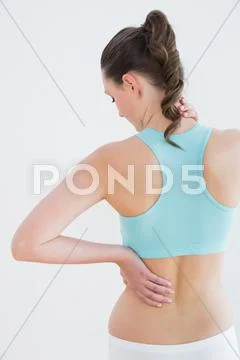 Rear view of a toned woman with back pain against wall Stock Photos