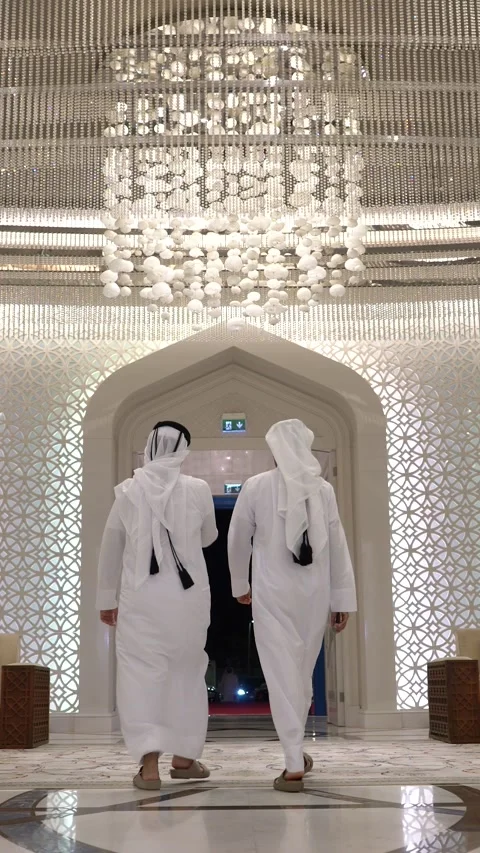 Rear view of two Arab men in white thobes walking side-by-side out of a Stockbeeldmateriaal 341143493
