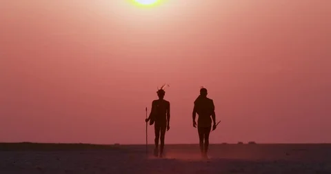 Rear view of two Bushman walking into the red sky of the setting sun on the Stock Footage 85250237