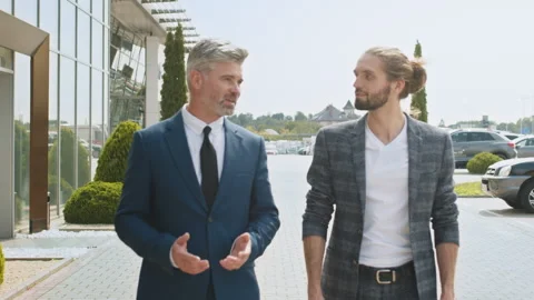 Rear view of two businessmen talking while walking on street in modern city. Two Stock Footage 240494589