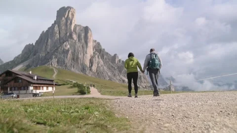 Rear view of two hikers approaching Cinque Torri via mountain trail in Stock Footage 318385320