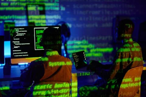 Rear view of two young programmers sitting in front of computers by desks Stock-Fotos