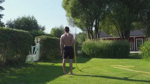 Rear view of well trained young man watering lawn using hosepipe Stock Footage 229639323