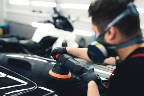 Rear view of white man in protective face mask polishing top of black car using Stock Photos