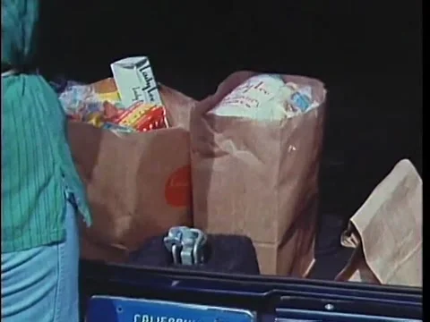 Rear view of woman taking groceries out of trunk of car, 1970s Stock Footage 64629939