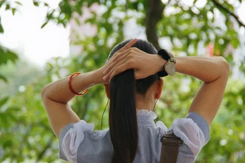 Rear view of woman tying ponytail while sitting at park Stock Photos