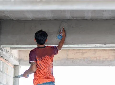 Rear view of a worker using a float trowel to smooth plaster on a concrete .. Stock Photos