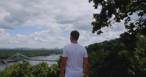 Rear view of young athletic man in white t-shirt stands on top of hill 스톡 동영상 159788466