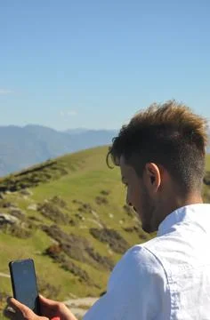 Rear view of a young guy taking photo of the mountain with his smartphone  Foto stock