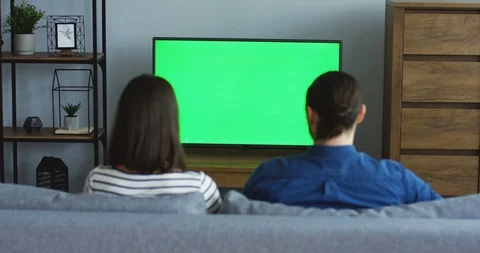 Rear view on the young man and woman sitting in front of the green screen of the Stock Footage 90207201