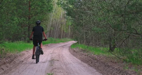 Rear view to the Young  man cyclist rides on a forest road.  Man in a Bicycle Vídeos de archivo 130769342