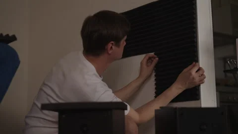 Rear view of young man mounting black acoustic foam panels on wall Stock Footage 342813452