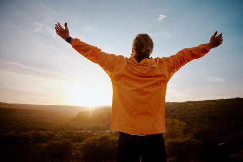 Rear view of young man standing on mountain with outstretched arms feeling Stock Photos