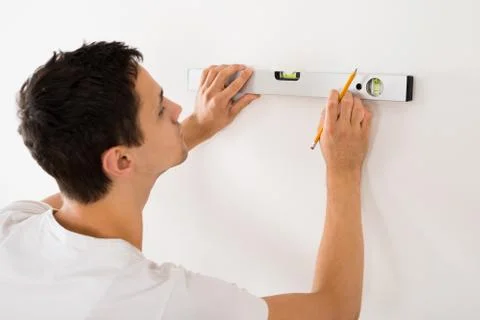 Rear view of young man using spirit level on white wall at home Foto stock