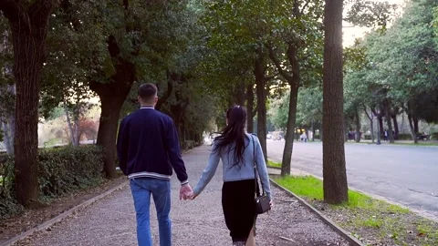Rear view. Young stylish hipster couple walks along the park alley. Stock Footage 135658250