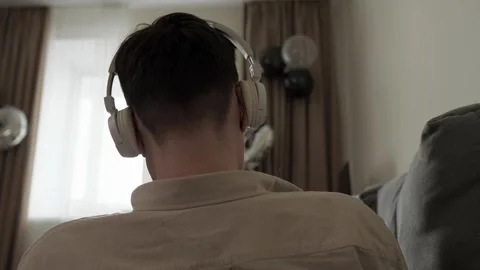Rear view of young unrecognisable man in wireless headphones listening to music Stock Footage 250614697