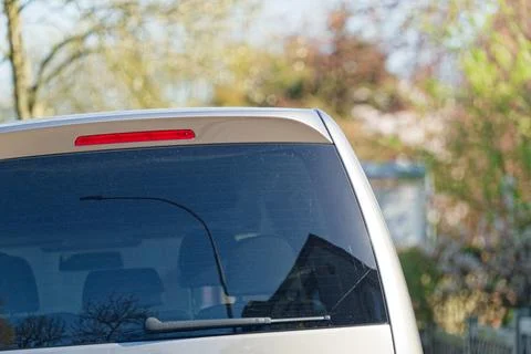Rear window of a silver car with a red brake light and wiper outdoors Stock Photos