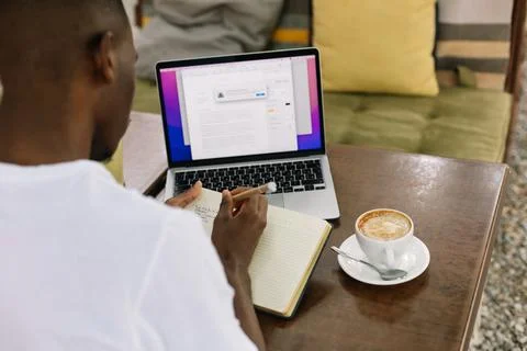 Rearview interracial man using laptop, writing notes in textbook and drinking 写真素材