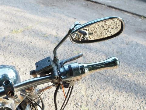 Rearview mirror on a rust-coated motorcycle handlebar with reflective asphalt in Stock Photos