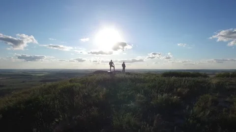 A receding drone view of the silhouettes of two people standing on a hilltop Stock Footage 130642937