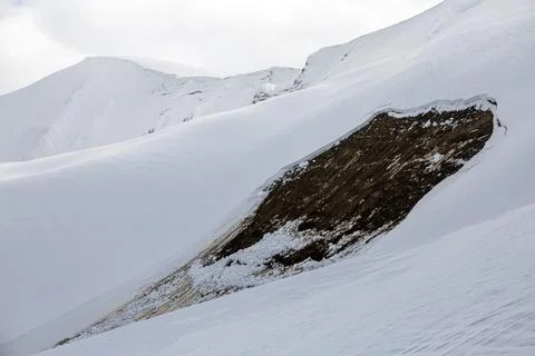A recent avalanche has exposed a dark patch of earth on a snow-covered moun.. Foto stock