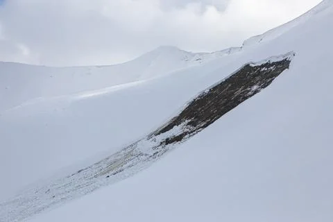 A recent avalanche has exposed a dark patch of earth on a snow-covered moun.. Stock Photos