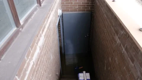 Recently flooded basement seen with a large pipe and pump used to pump out Stock Footage 231195107