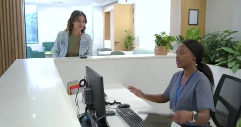 Receptionist in scrubs checking tablet after woman showing phone at clinic desk Stock Footage 341090028