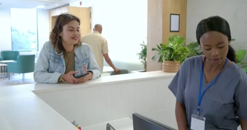 Receptionist in scrubs reaching for terminal on client presenting phone at Stock Footage 340964505