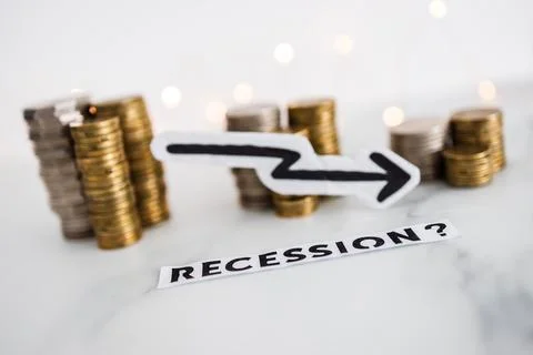 Recession text with arrow going down in front of decreasing stacks of coins r Stock Photos