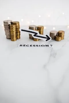 Recession text with arrow going down in front of decreasing stacks of coins r Stock Photos
