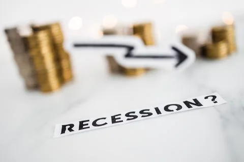 Recession text with arrow going down in front of decreasing stacks of coins r Stock Photos
