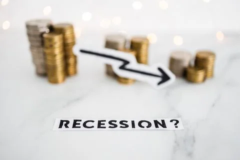 Recession text with arrow going down in front of decreasing stacks of coins r Stock Photos