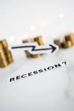 Recession text with arrow going down in front of decreasing stacks of coins r Stock Photos