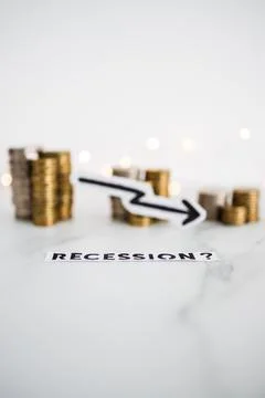Recession text with arrow going down in front of decreasing stacks of coins r Stock Photos