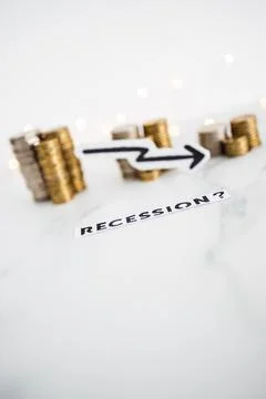 Recession text with arrow going down in front of decreasing stacks of coins r Stock Photos