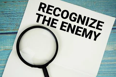 Recognize The Enemy text written on notepad with magnifying glass flat lay .. Stock Photos