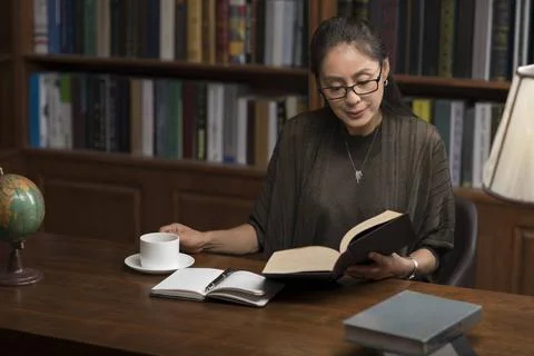 RECORD DATE NOT STATED Elegant mature Chinese woman reading book in study ... 스톡 사진