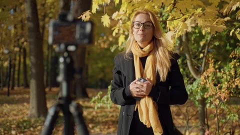 Records video report with red-haired woman in glasses in autumn park Stock Footage 163613207