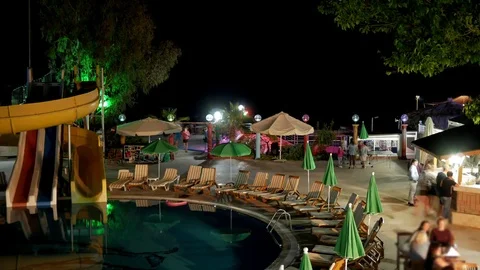 Recreation area with a hotel pool at night. People quickly go to the bar and Stock Footage 76476809