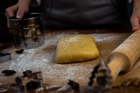 A rectangle of dough lies on baking parchment, a rolling pin and cookie cutters Stock Photos