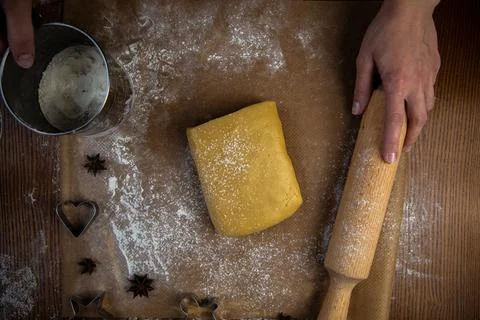A rectangle of dough lies on baking parchment, a rolling pin and cookie cutters Stock Photos