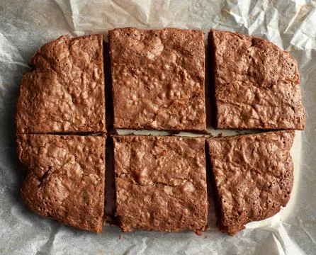 Rectangular baked brownie chocolate cake with cracked surface on white parchm Stock Photos