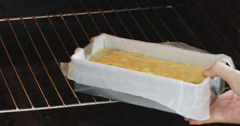 A rectangular baking dish with yellow dough is placed in the oven with one hand Stock Footage 151737888